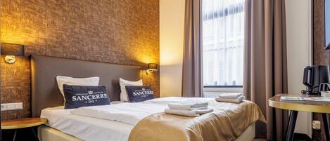 A hotel room with a large bed, two pillows, a bedside table, a television, and a window with curtains.