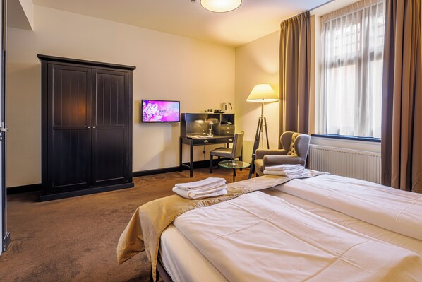 Una habitación de hotel con cama, escritorio, televisor, silla y armario.