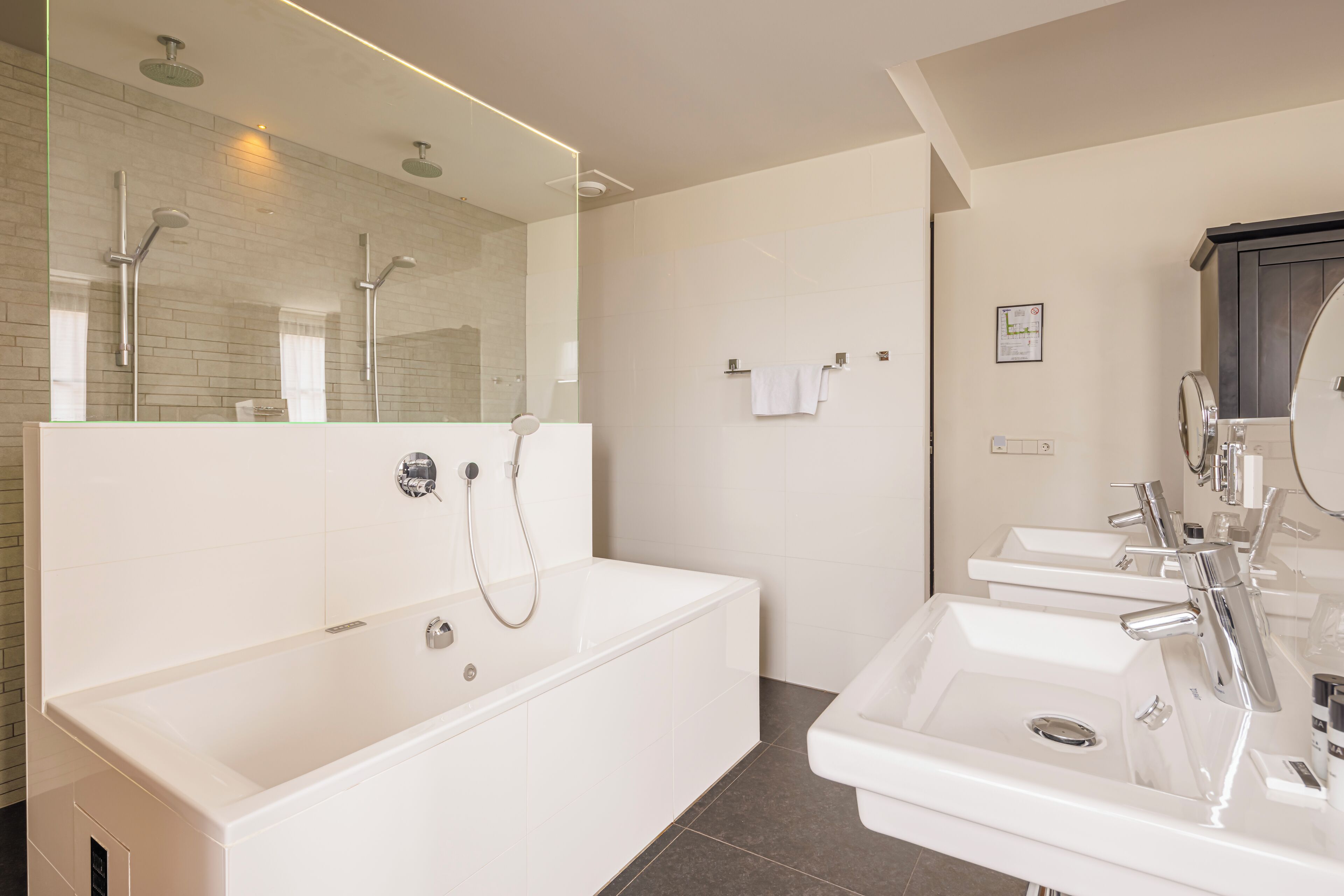 Een moderne badkamer met een ruime badkuip, een aparte douche en een wastafel met twee kommen.