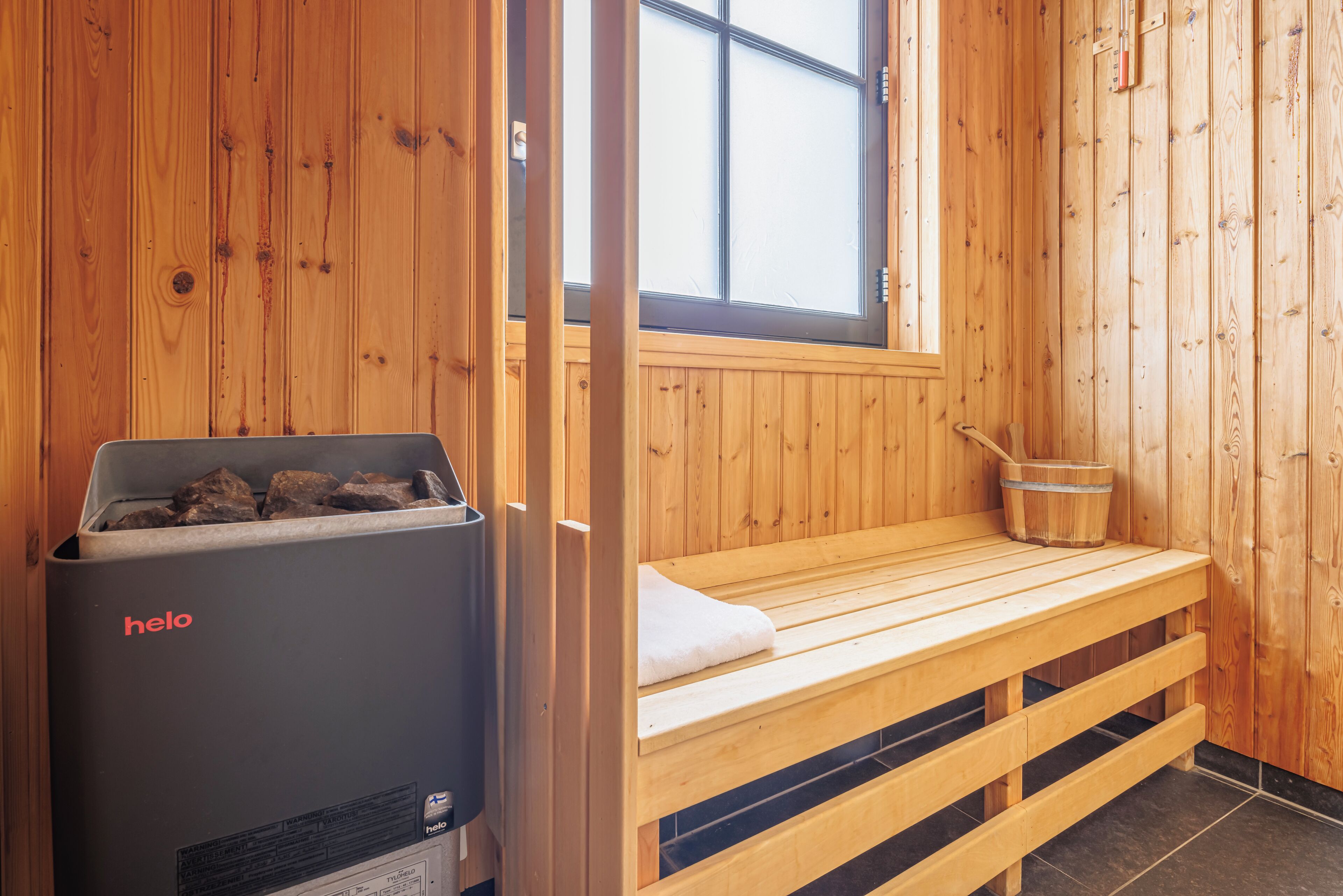 Una sauna de madera con un banco, un cubo y un calentador que dice 'helo'.