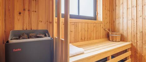 Una sauna de madera con un banco, un cubo y un calentador que dice 'helo'.