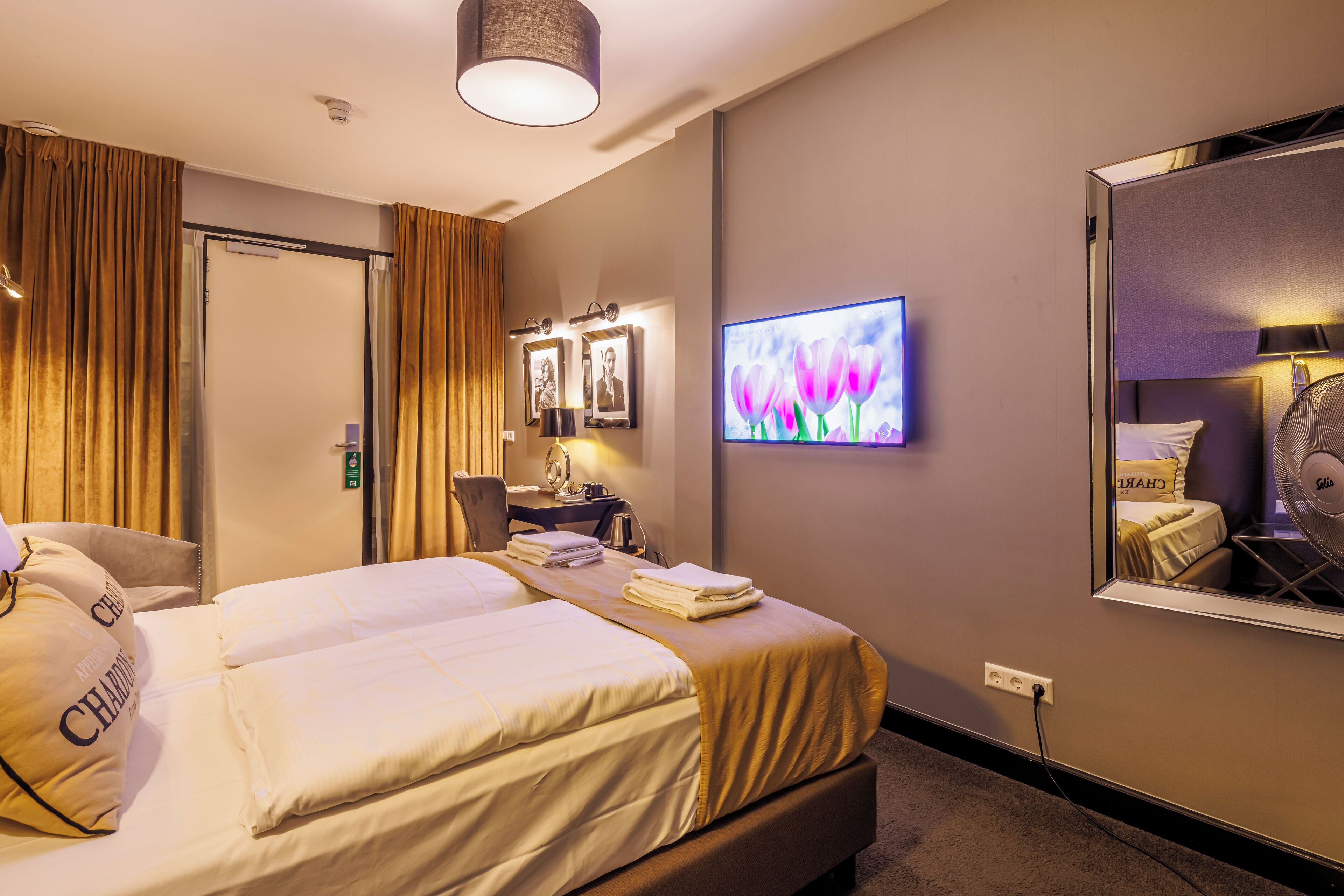 Habitación de hotel con una cama grande, un escritorio, una silla, un televisor y un espejo.