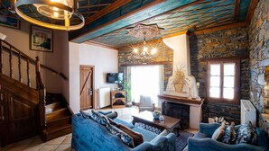 Una sala rústica con chimenea de piedra, sofás tapizados en azul, una escalera de madera y un techo con vigas a la vista.