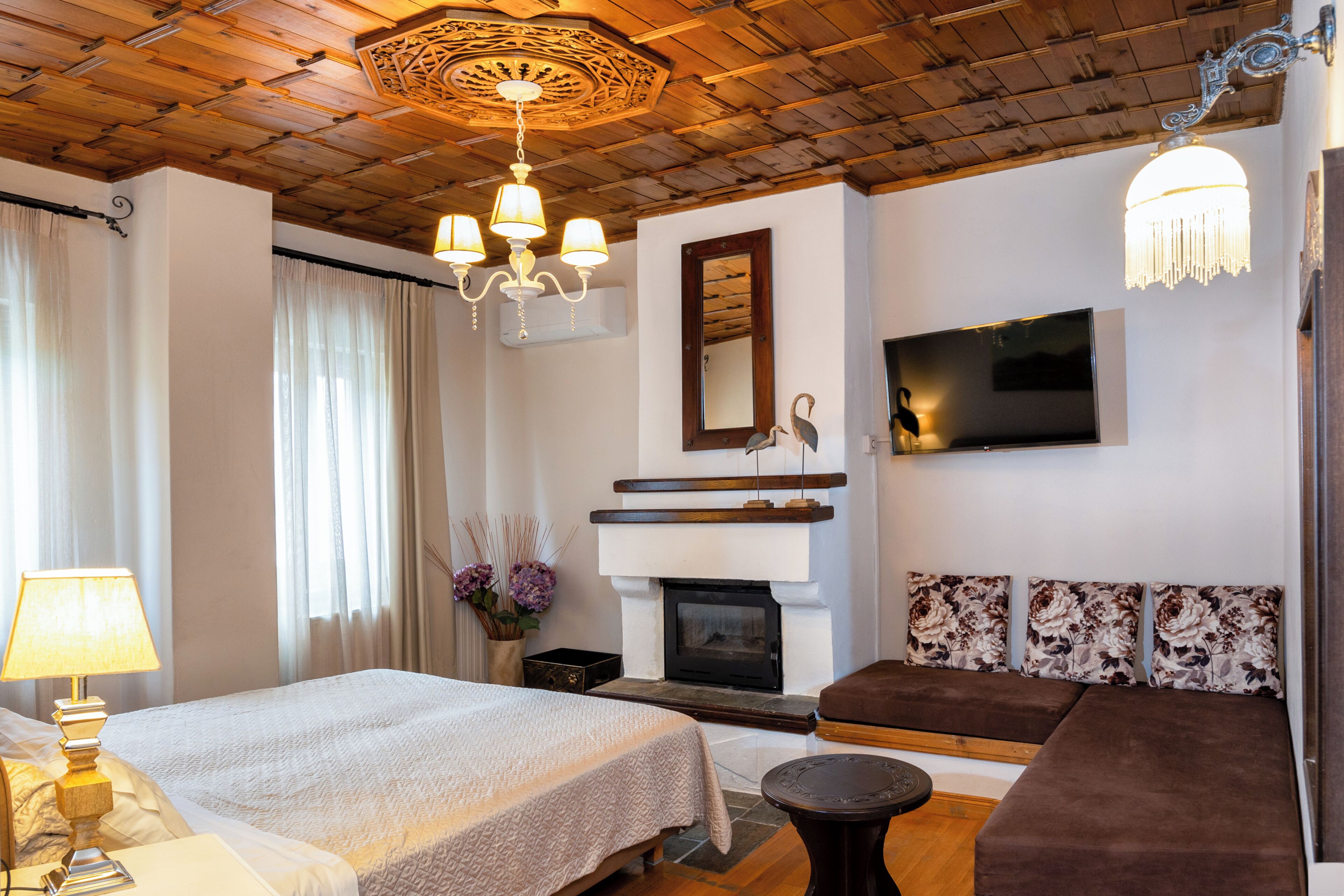 A hotel room with a bed, a sofa, a fireplace, a TV, and a chandelier.