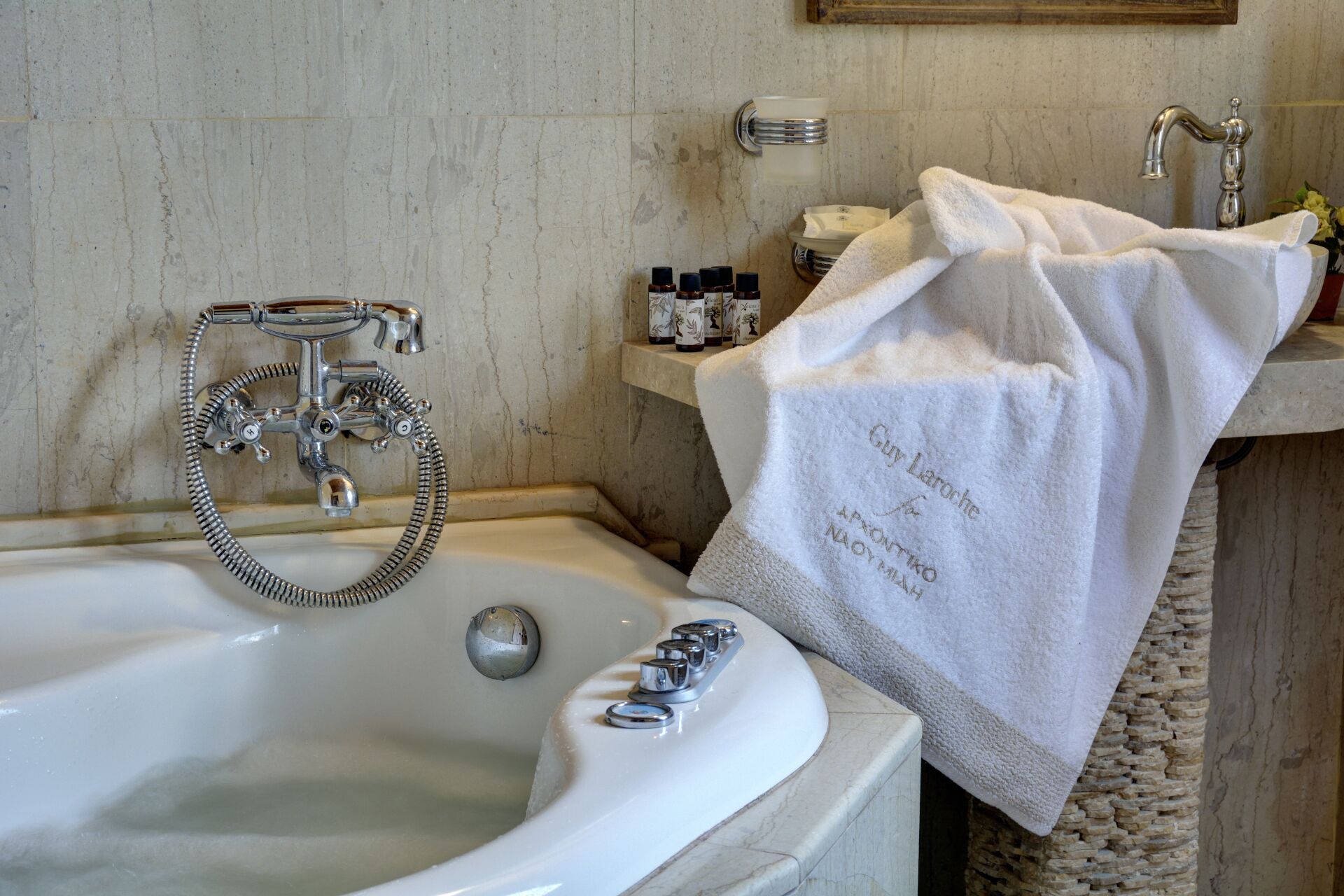 Une salle de bain avec une baignoire, une douche et un lavabo. On trouve des articles de toilette sur l’étagère et une serviette est accrochée au mur.