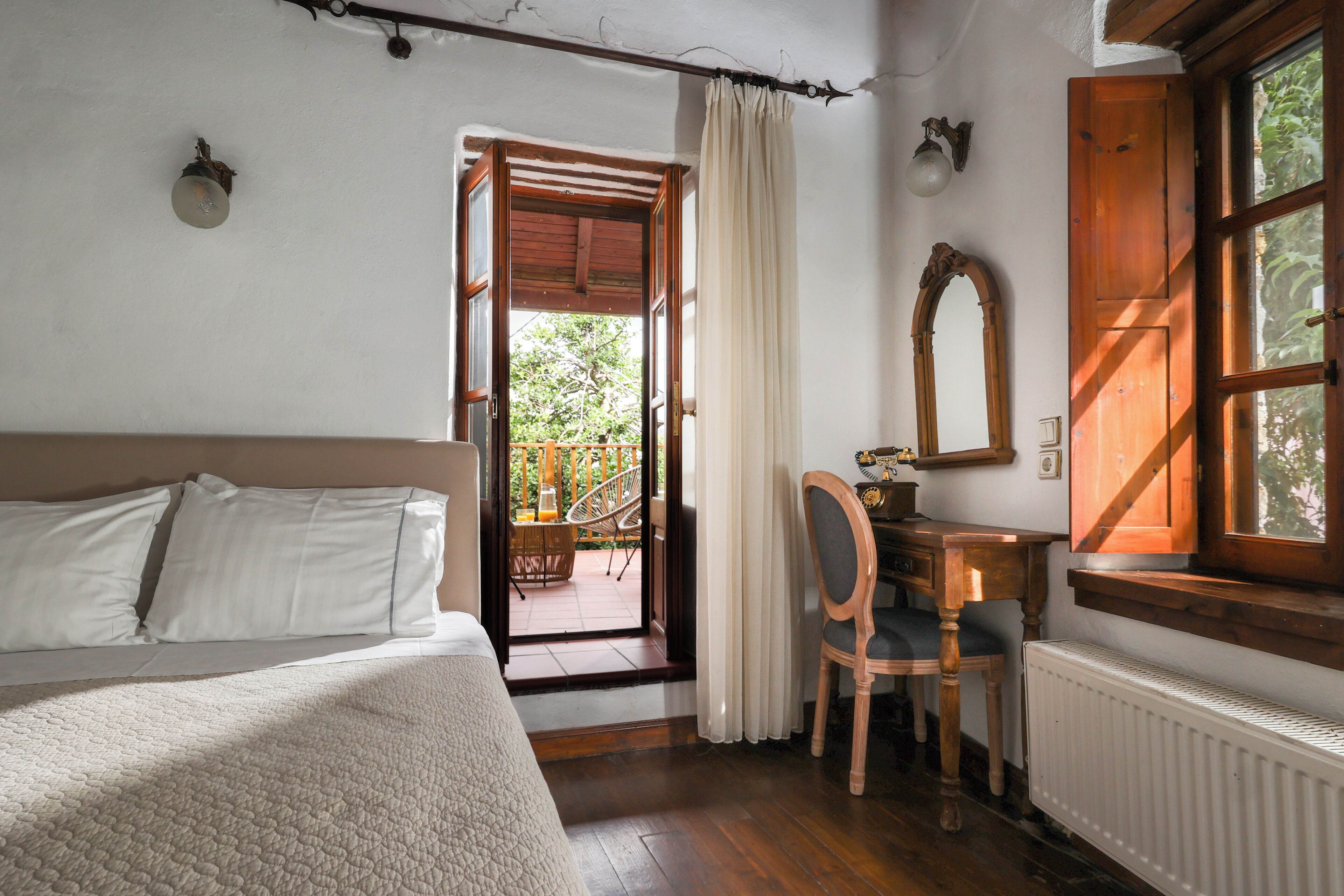 A bedroom with a bed, a desk, a chair, a window, and a door leading to an outdoor area.