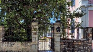 Una entrada protegida por muros de piedra, una reja metálica y un árbol que da sombra.