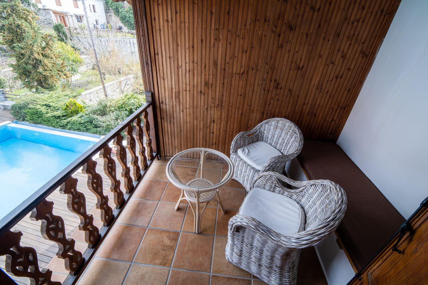 A balcony with a pool, wicker chairs, and a view of greenery.