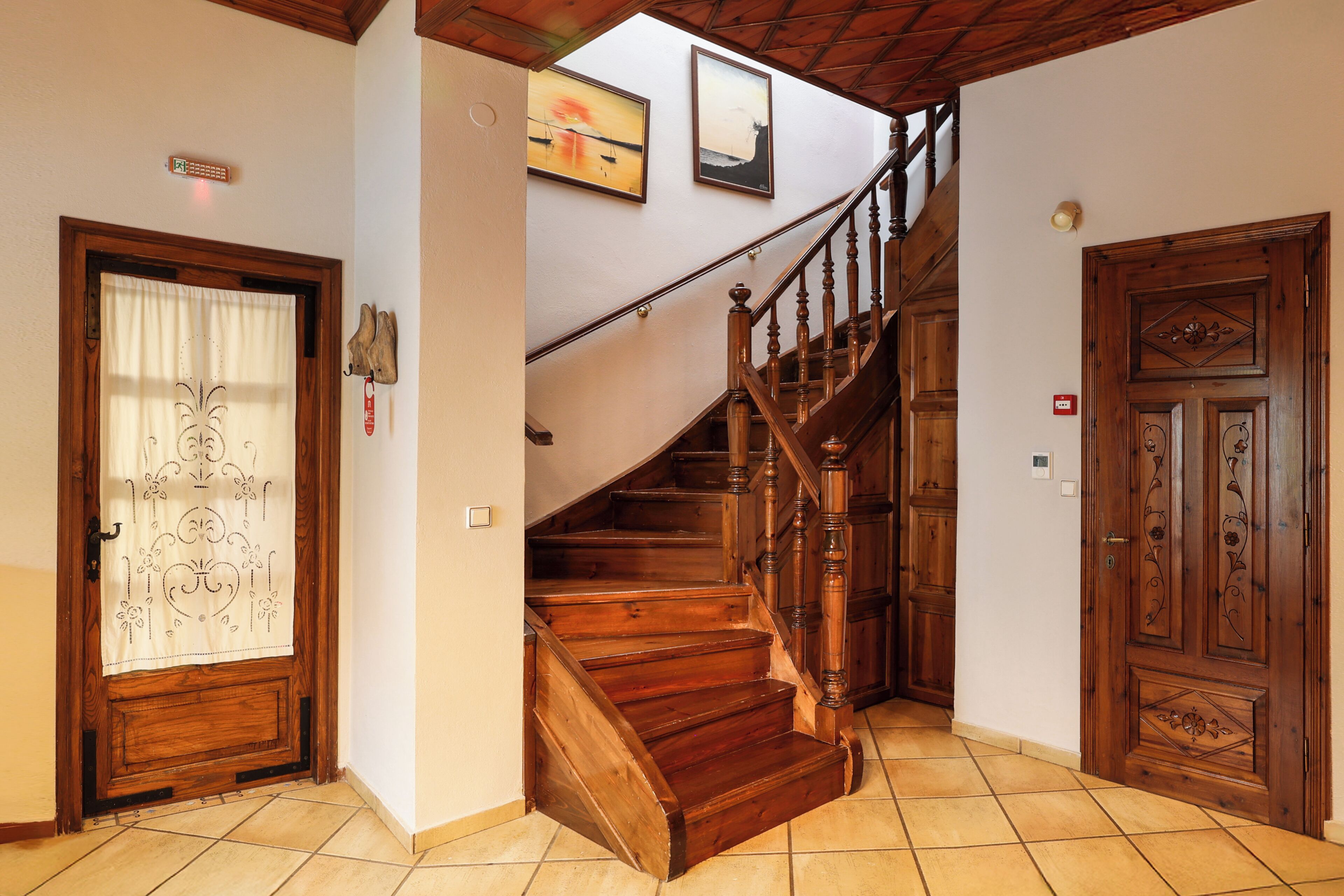 Una escalera de madera conduce a un piso superior, una puerta de madera con un panel decorativo y un suelo de baldosas.