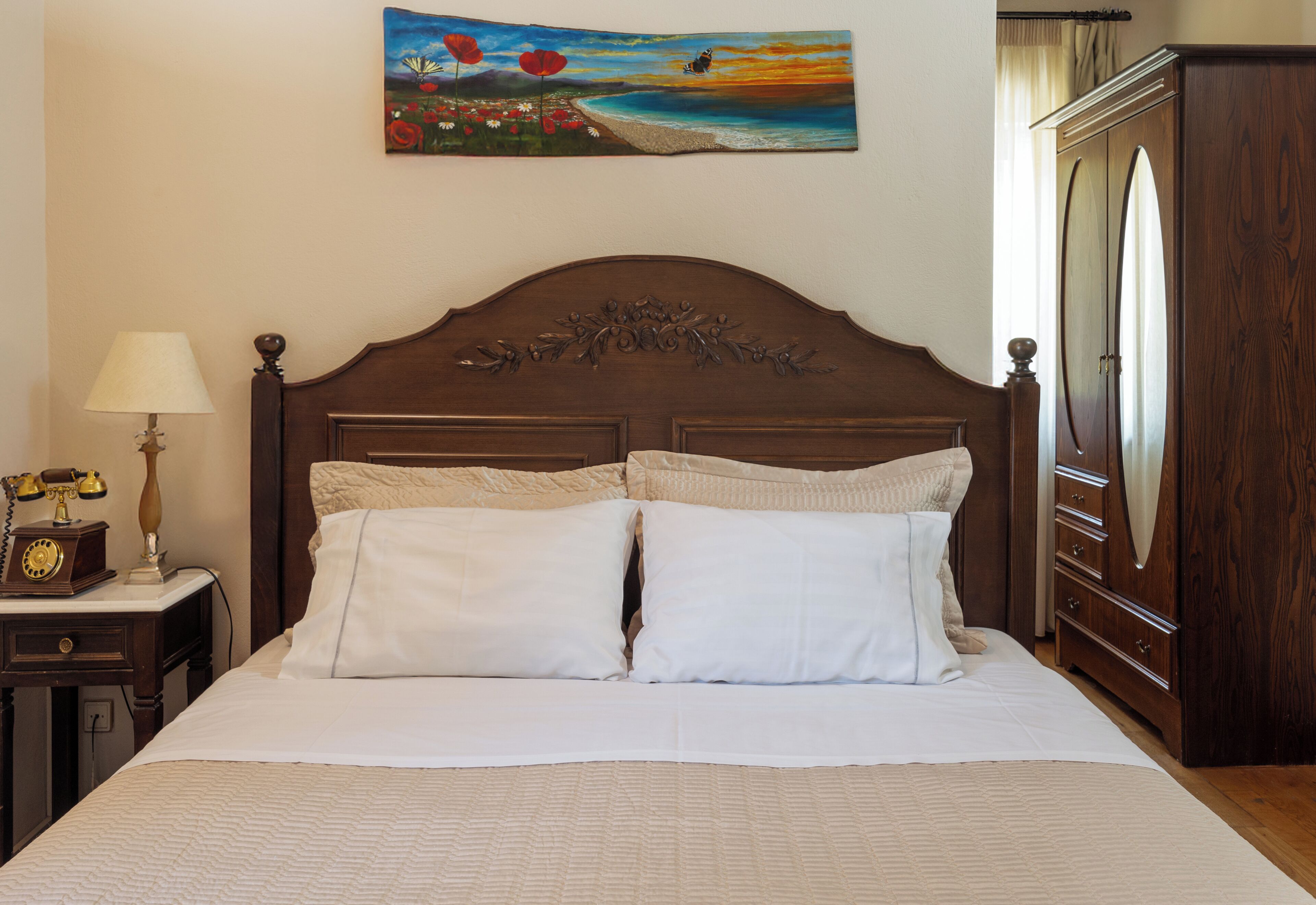 A neatly made bed with a headboard, a bedside table with a lamp, and a painting on the wall.