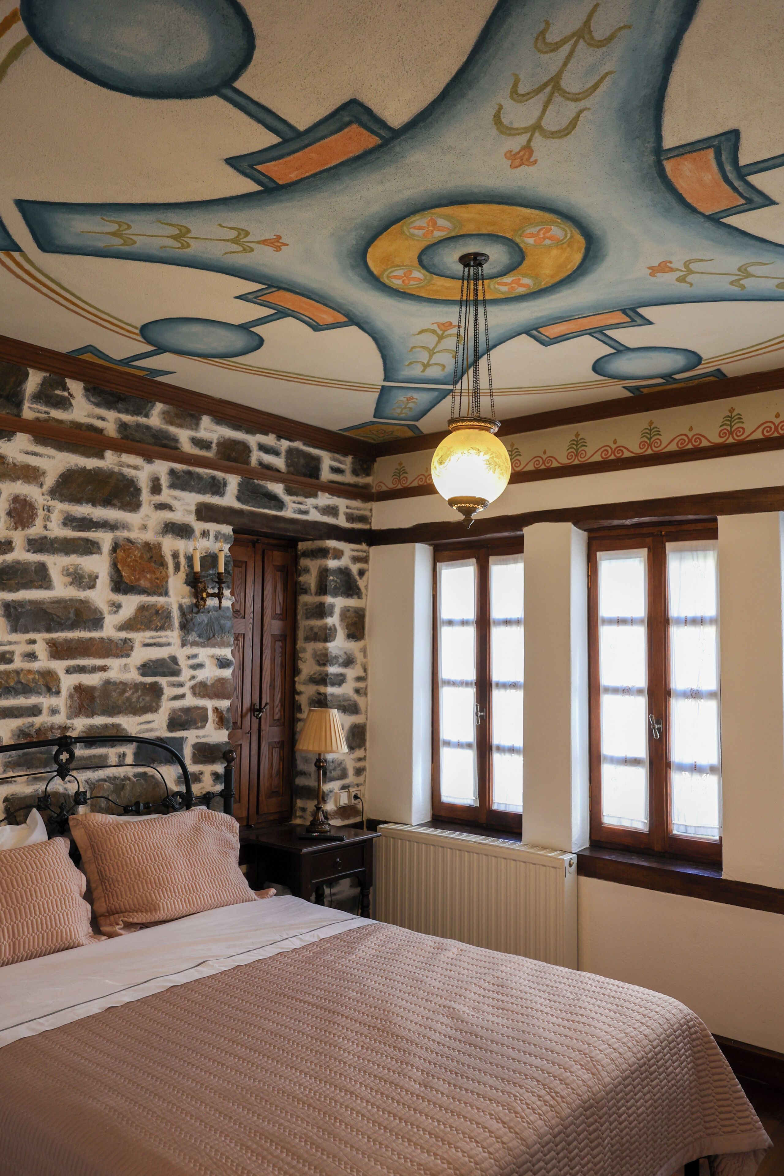 Una habitación con pared de piedra, una cama con cubrecama color beige, una puerta de madera y una ventana con vistas.