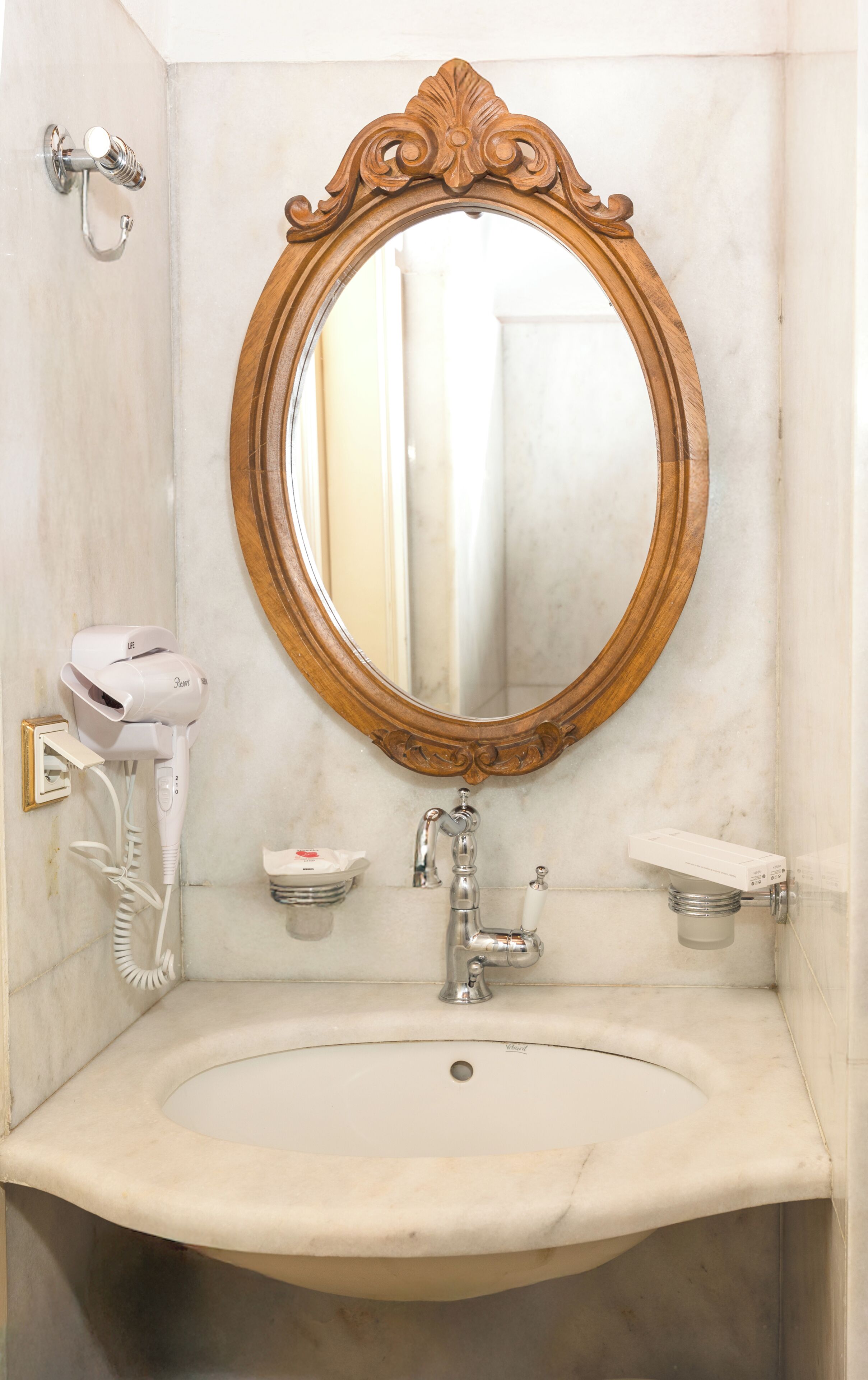 A bathroom with a marble sink, a hairdryer, a mirror with an ornate frame, and a towel rack.