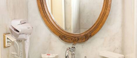 A bathroom with a marble sink, a hairdryer, a mirror with an ornate frame, and a towel rack.