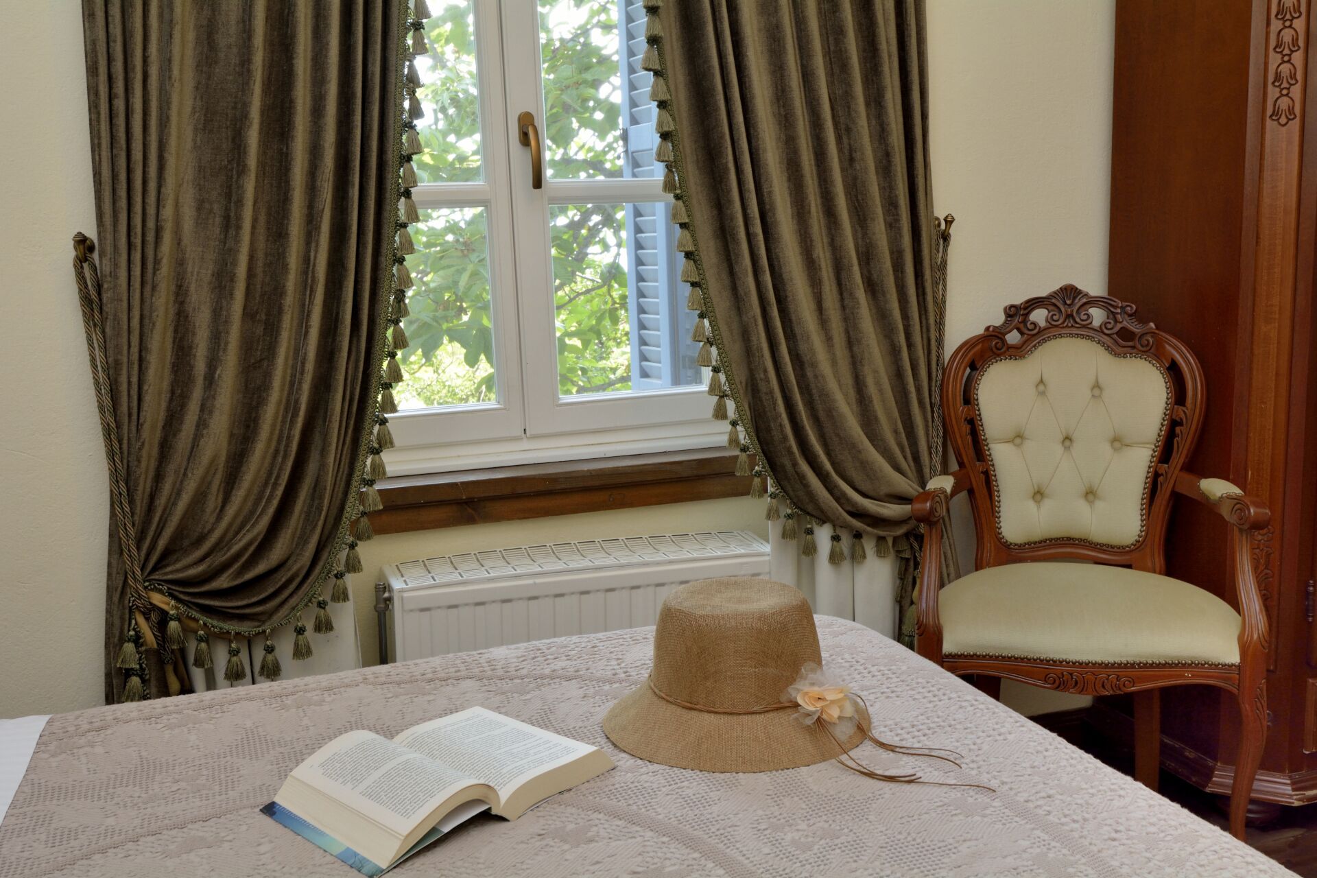 Una habitación con ventana, radiador, una silla de madera y un libro abierto sobre una mesa.