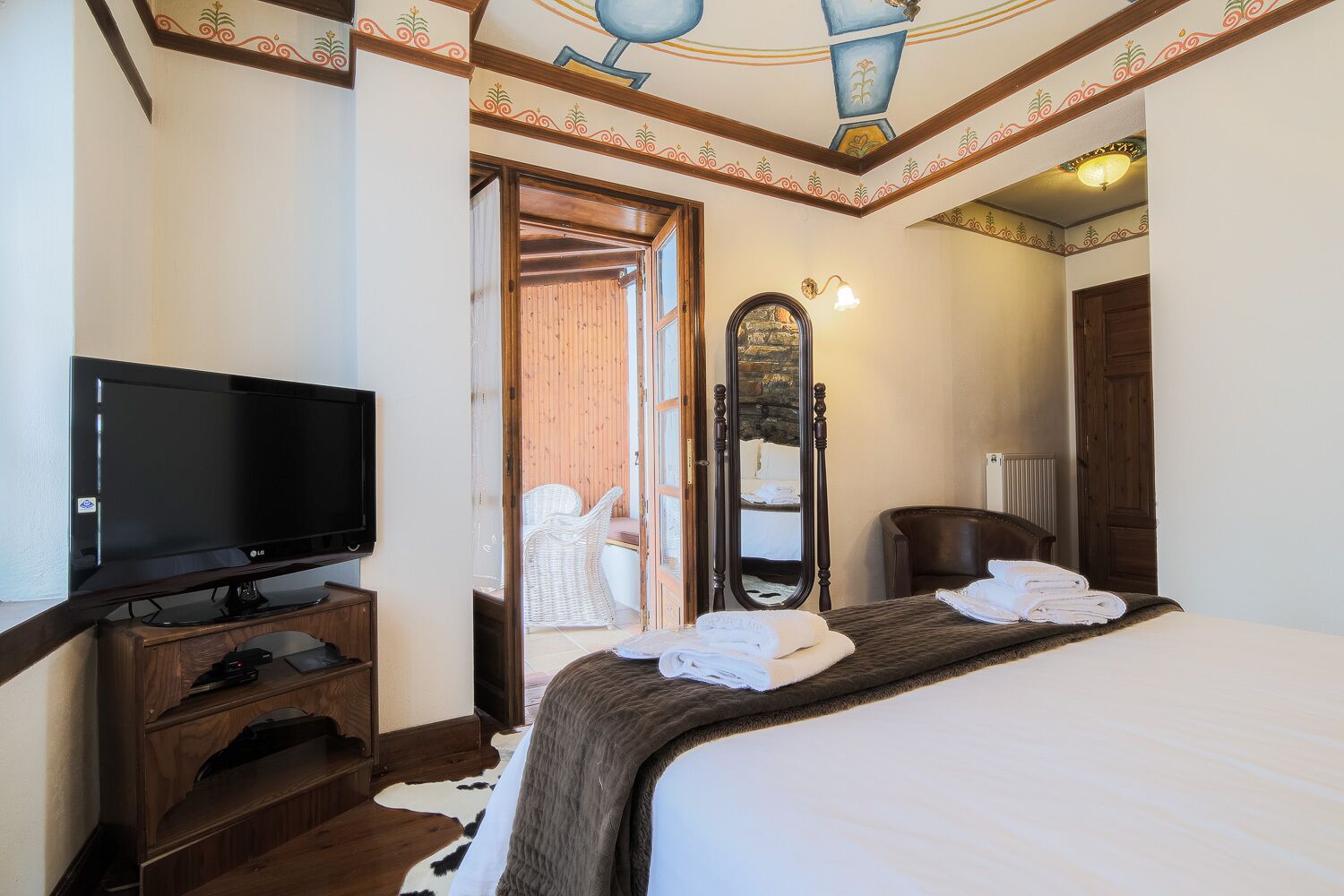 Une chambre d’hôtel avec un lit, une télévision, un miroir et une commode en bois.