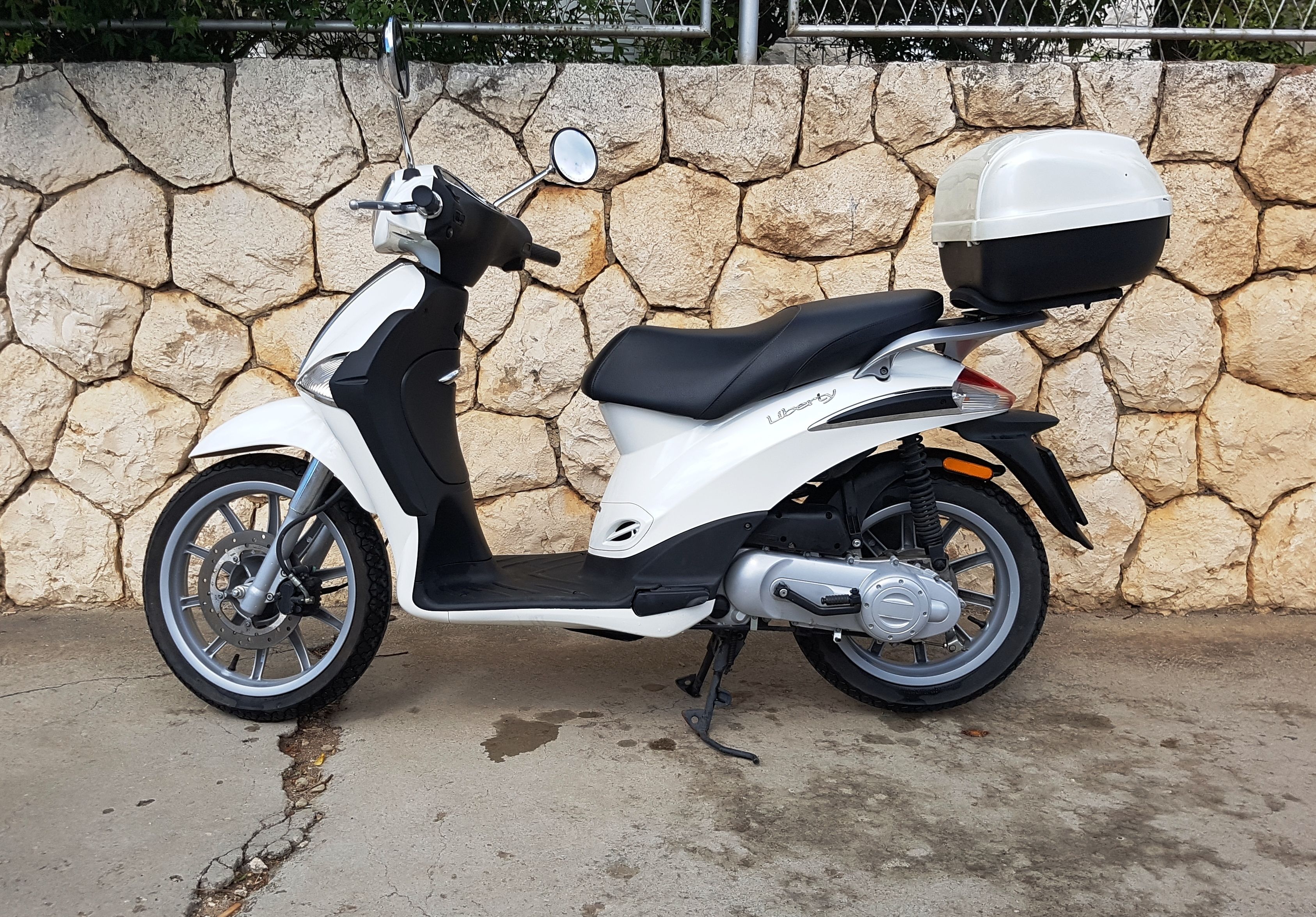 En hvid scooter med opbevaringskasse parkeret op ad en stenvæg.