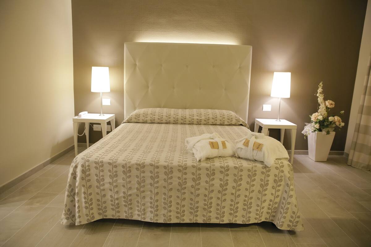 A neatly made bed with a patterned bedspread, two bedside lamps, and a vase with flowers on the right.