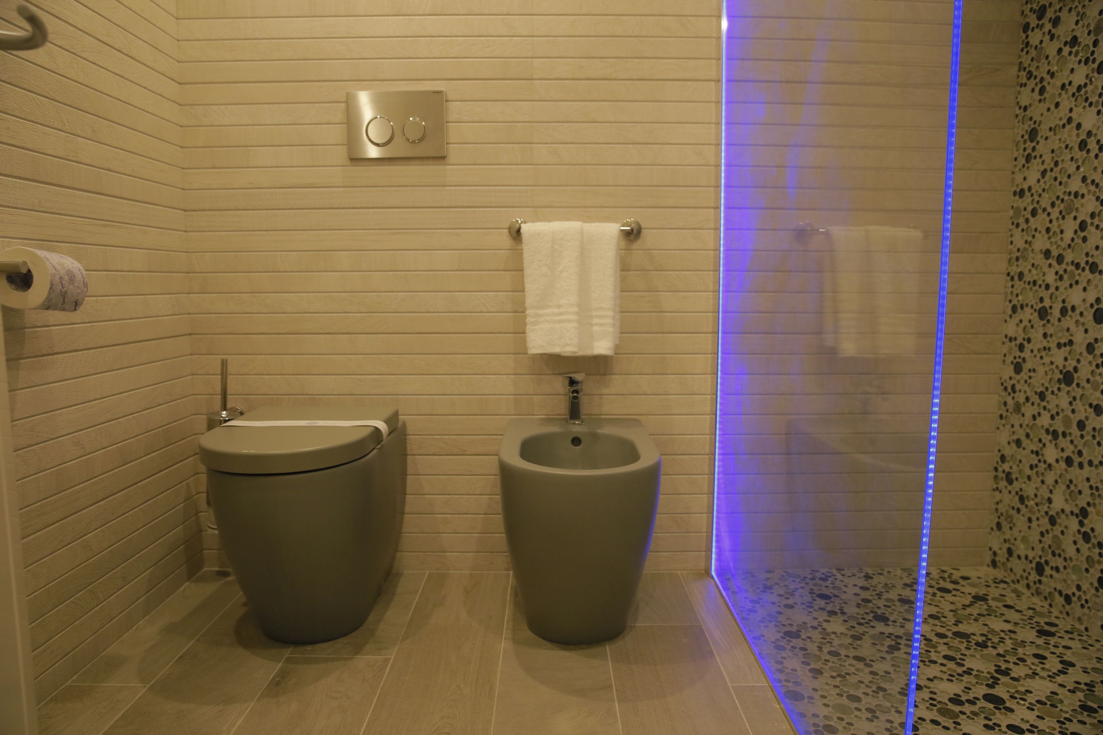 A modern bathroom with two urinals, a toilet, and a shower area with a blue light.