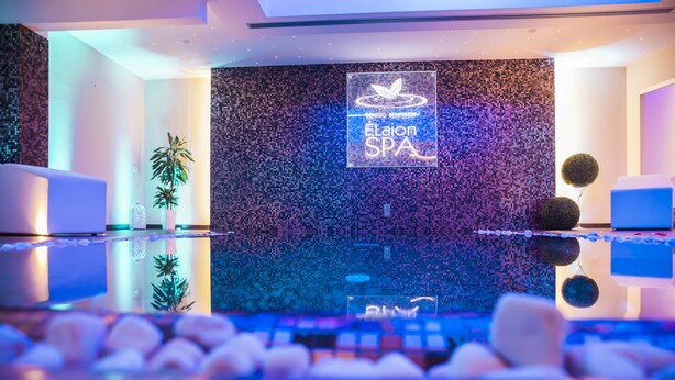 Un moderno espacio de spa con una pared de mosaicos, un mostrador de recepción y una zona de estar con camillas de masaje.