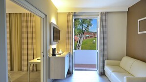 Habitación de hotel con sofá, televisor, escritorio y vistas a un jardín a través de una puerta corredera.