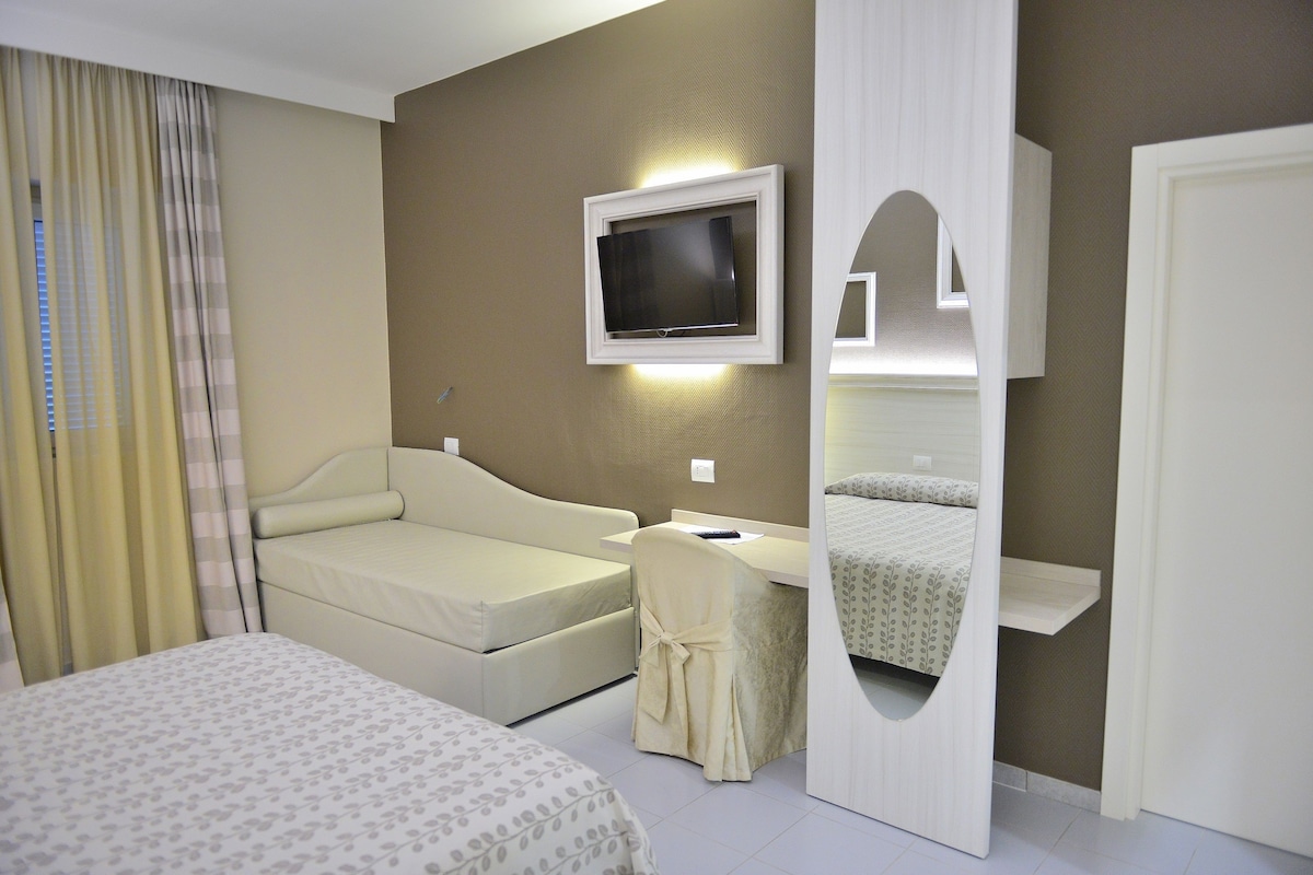 A hotel room with a bed, a desk, a television, and a mirror.