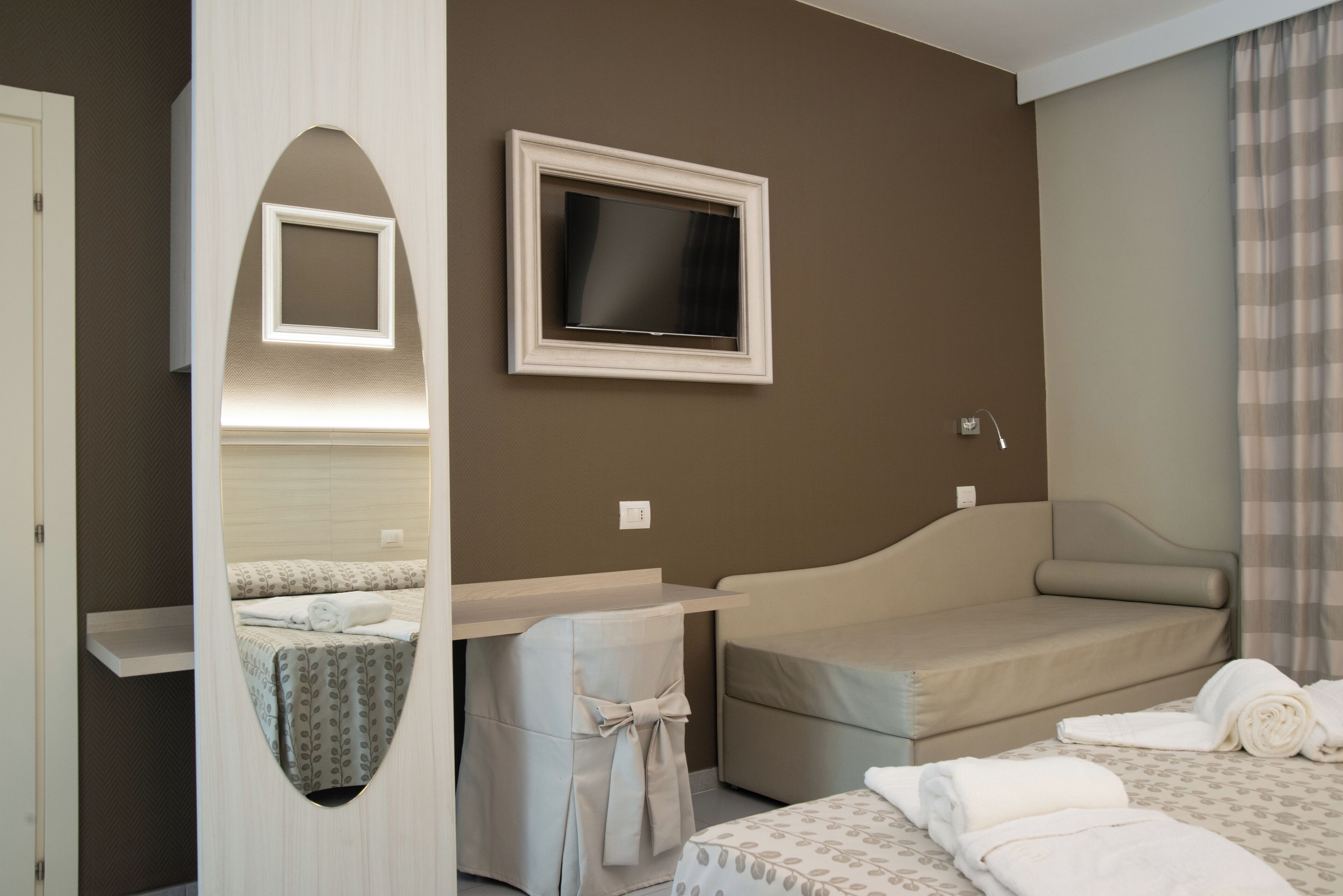 Une chambre d’hôtel comprenant un lit, un téléviseur fixé au mur, un bureau avec une chaise et un miroir.