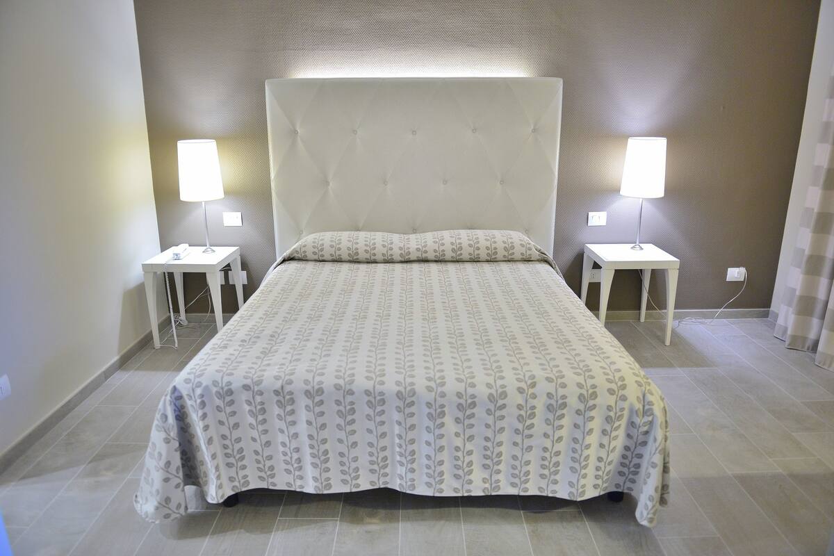 A neatly made bed with a patterned bedspread, two bedside tables with lamps, and a wall with a textured pattern.