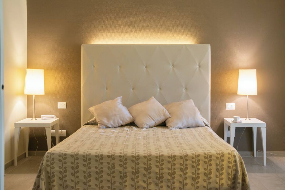 A hotel room with a large bed, two bedside tables, and two lamps.