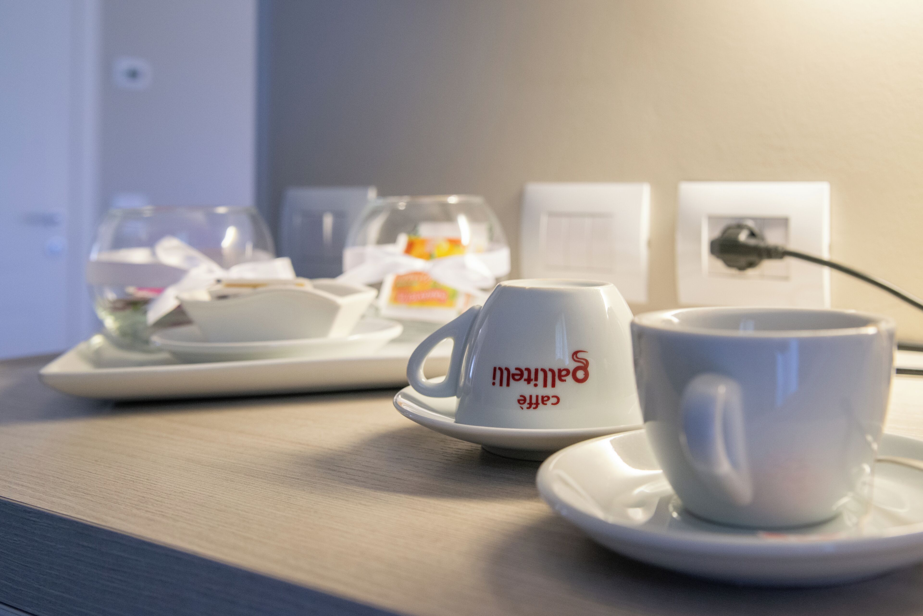 A hotel room with a table set for breakfast, including a cup with "Bartonby" written on it, a glass of water, and a plate with food items.