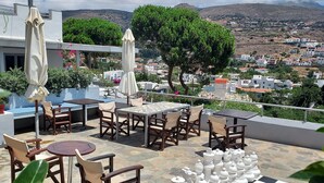 A terrace with outdoor seating, a chessboard, and a view of a hillside town. - Villa Arni (Andros)