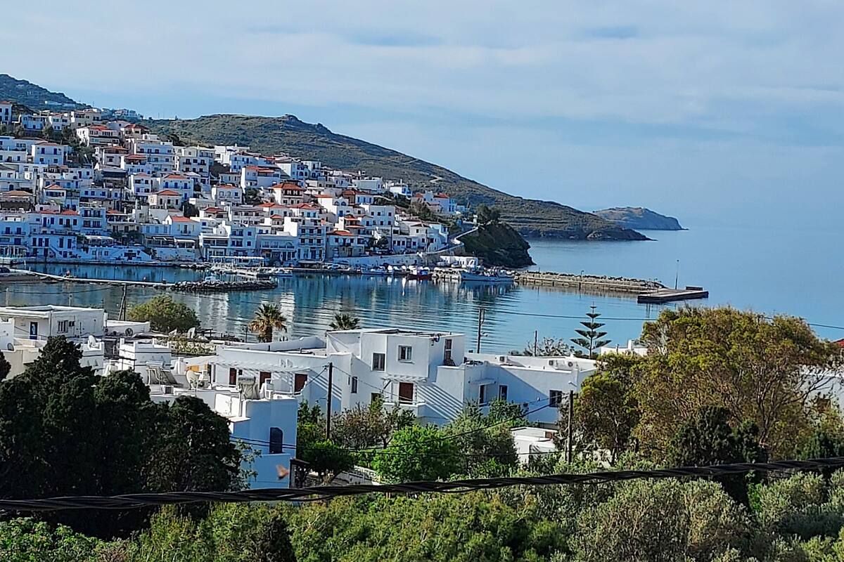 Un pueblo costero con edificios blancos, un puerto deportivo y un paisaje montañoso al fondo.