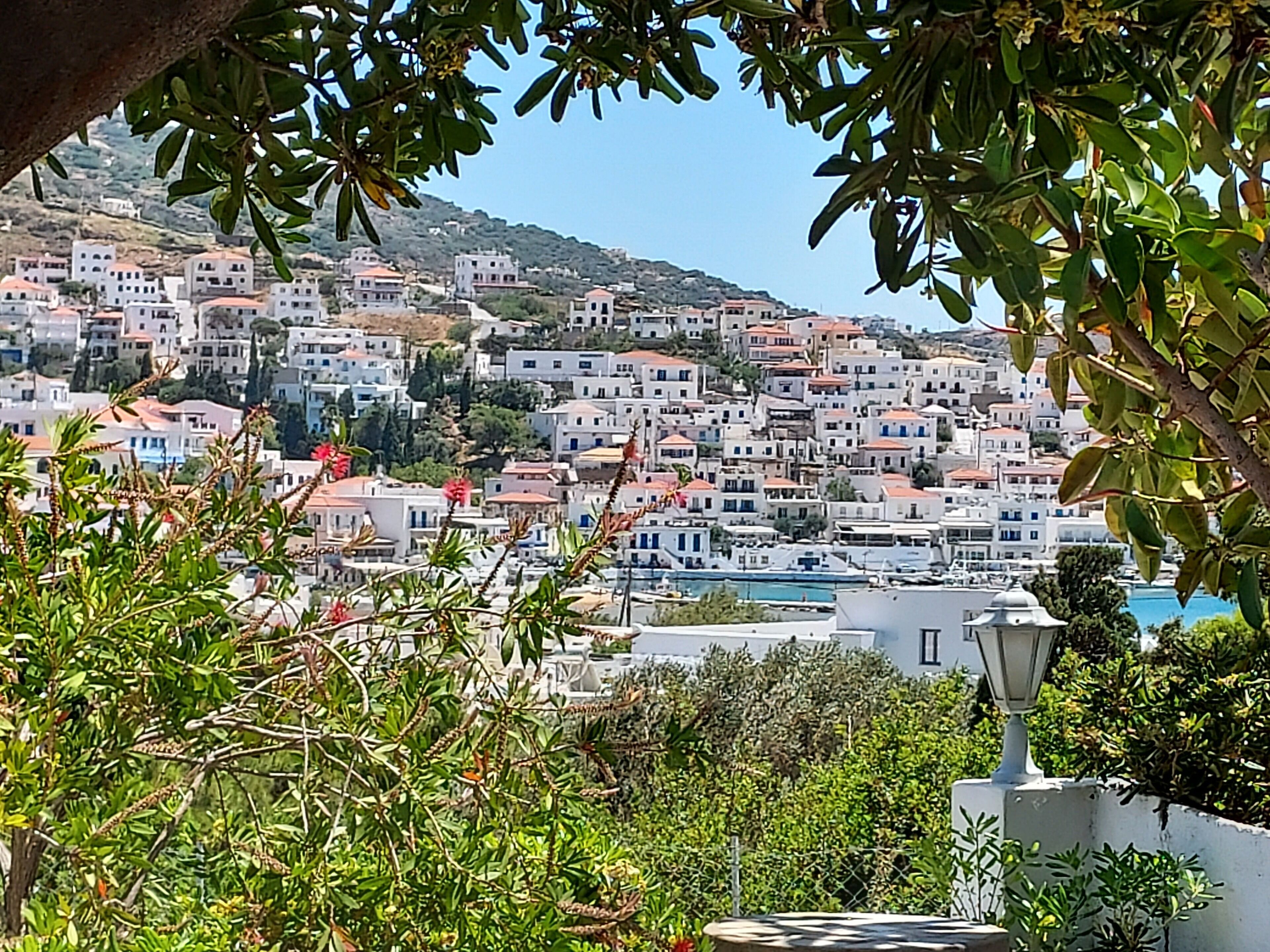 Un pueblo costero con edificios blancos y tejados rojos, rodeado de vegetación y colinas.