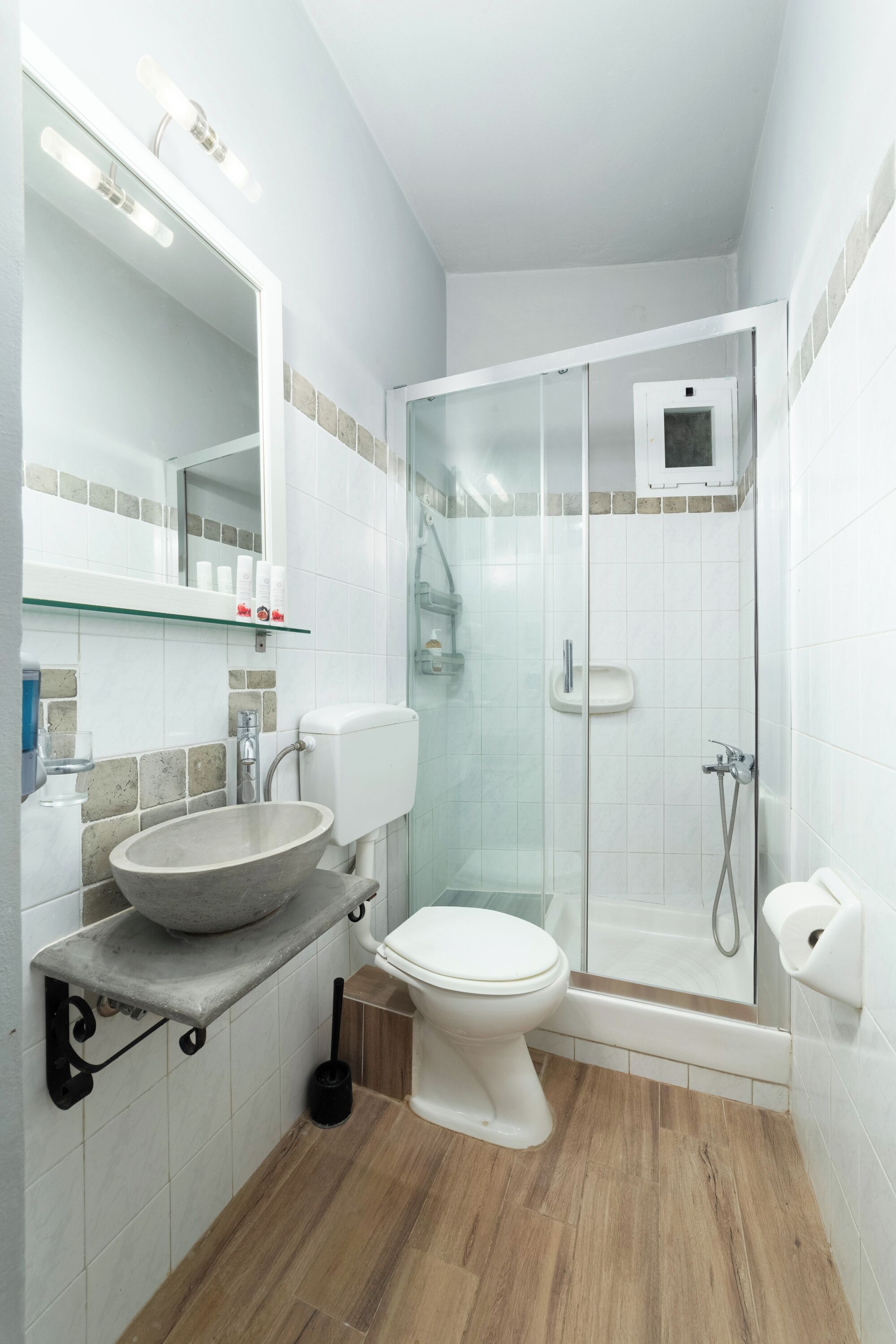 A modern bathroom with a large mirror, a vessel sink, a toilet, and a glass-enclosed shower.
