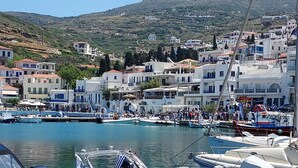 A marina with boats docked, a crowd of people, and buildings in the background. - Villa Arni (Andros)