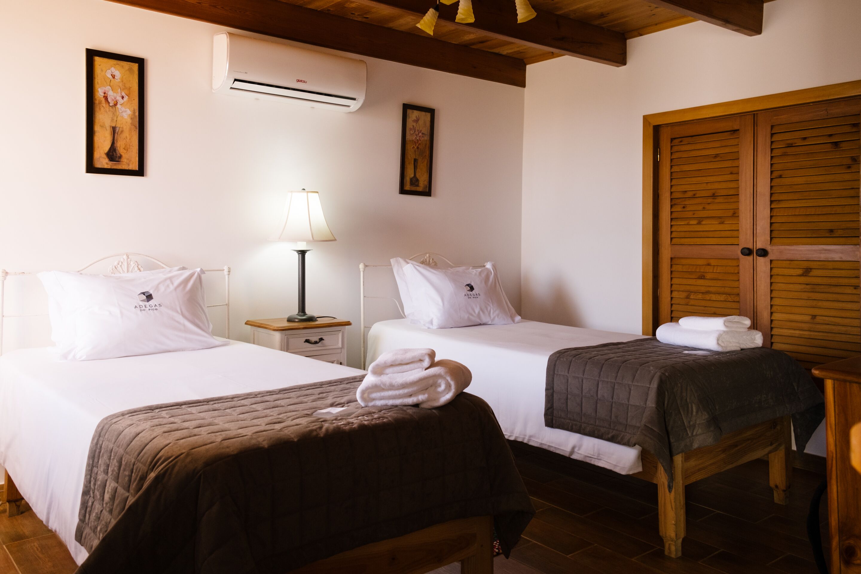 A hotel room with two beds, a wooden bench, an air conditioning unit, and a wooden door.