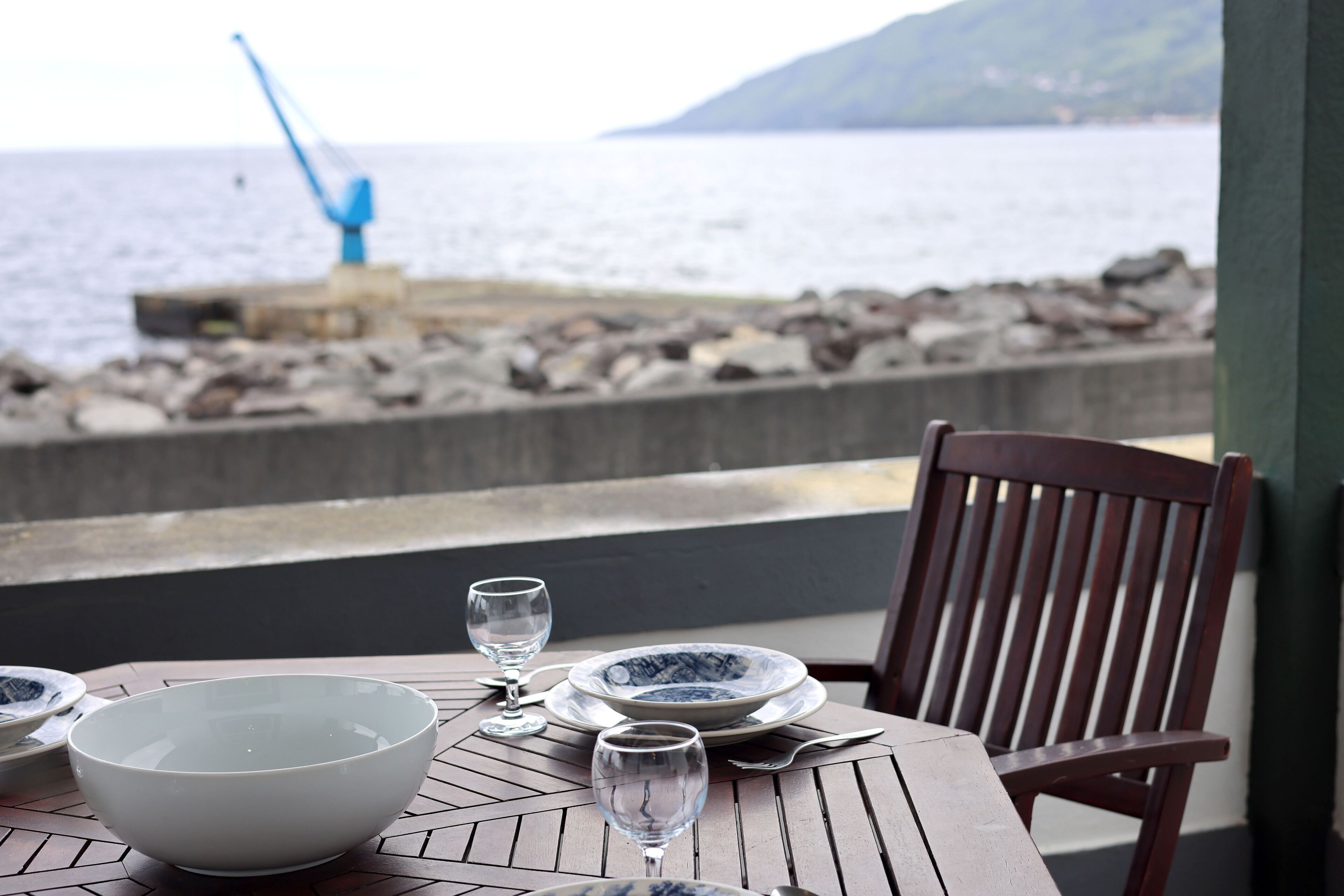 A table set with plates, bowls, and wine glasses, overlooking a rocky shoreline and the sea.