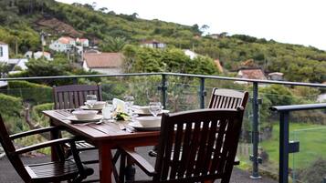 A dining table set with plates, glasses, and cutlery, overlooking a lush green landscape with houses in the background.