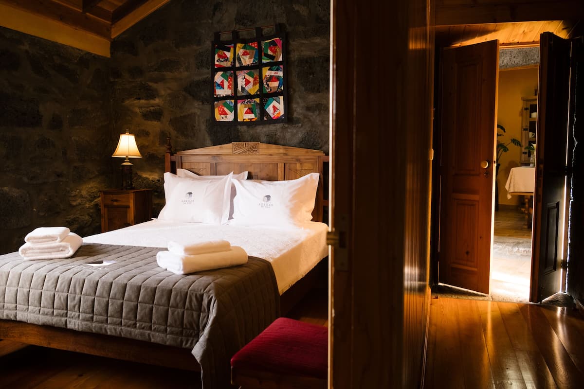 A wooden bed with a quilted bedspread, a nightstand with a lamp, and a wall with a quilt pattern.