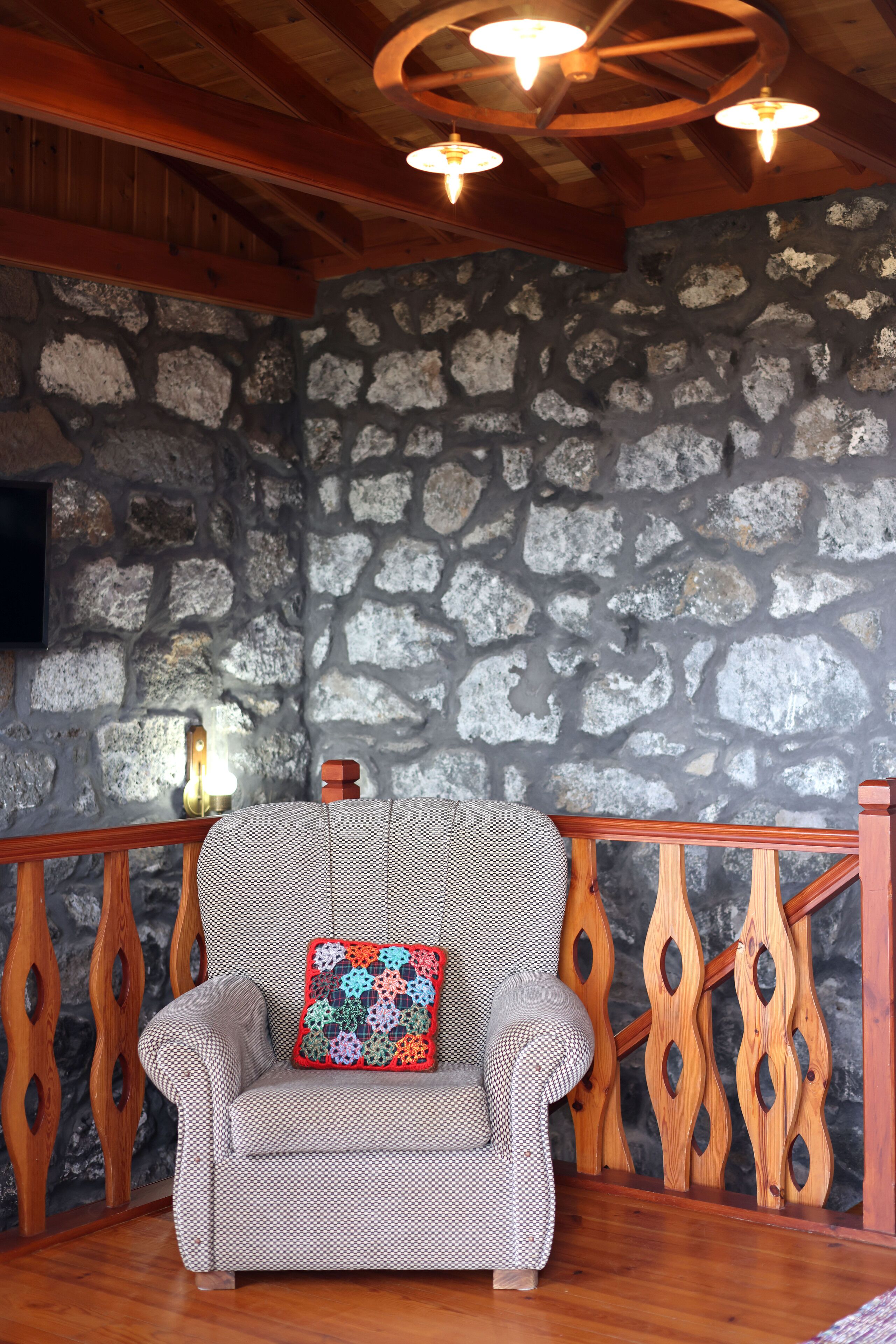 Une pièce chaleureuse avec un mur en pierre, un plafond en bois et une chaise en bois agrémentée d’un coussin à motifs.