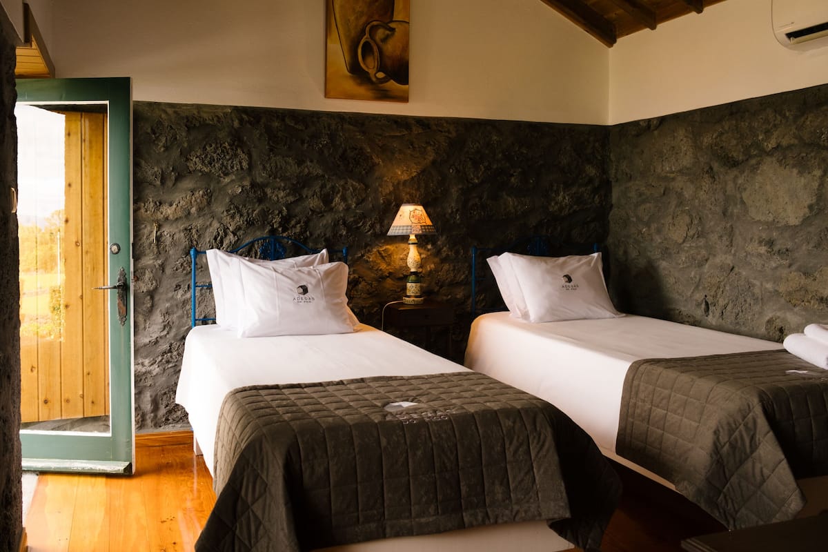 A room with two beds, a stone wall, a wooden door, and a lamp.