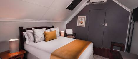 Un dormitorio con cama, lámparas de noche, mesita de noche, una silla, una puerta y un cuadro en la pared.