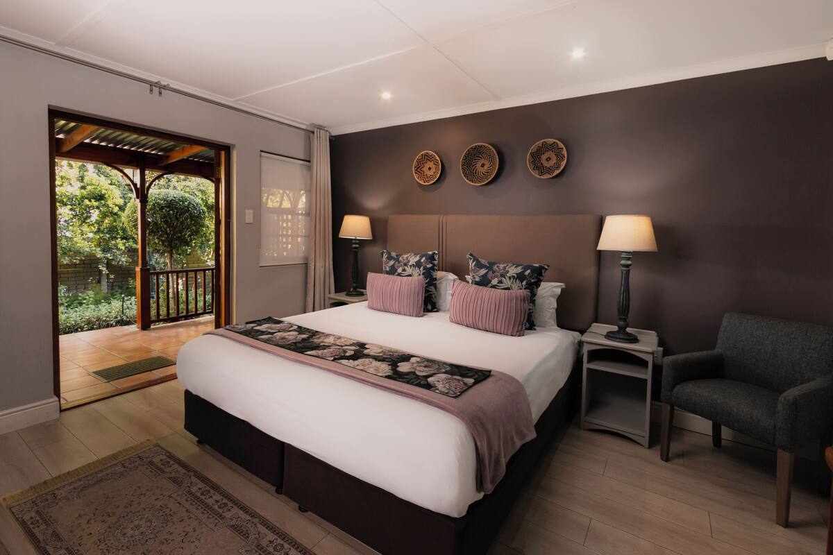 Quarto com uma cama grande, duas mesas de cabeceira com abajures, uma cadeira e vista para o exterior por uma porta deslizante.