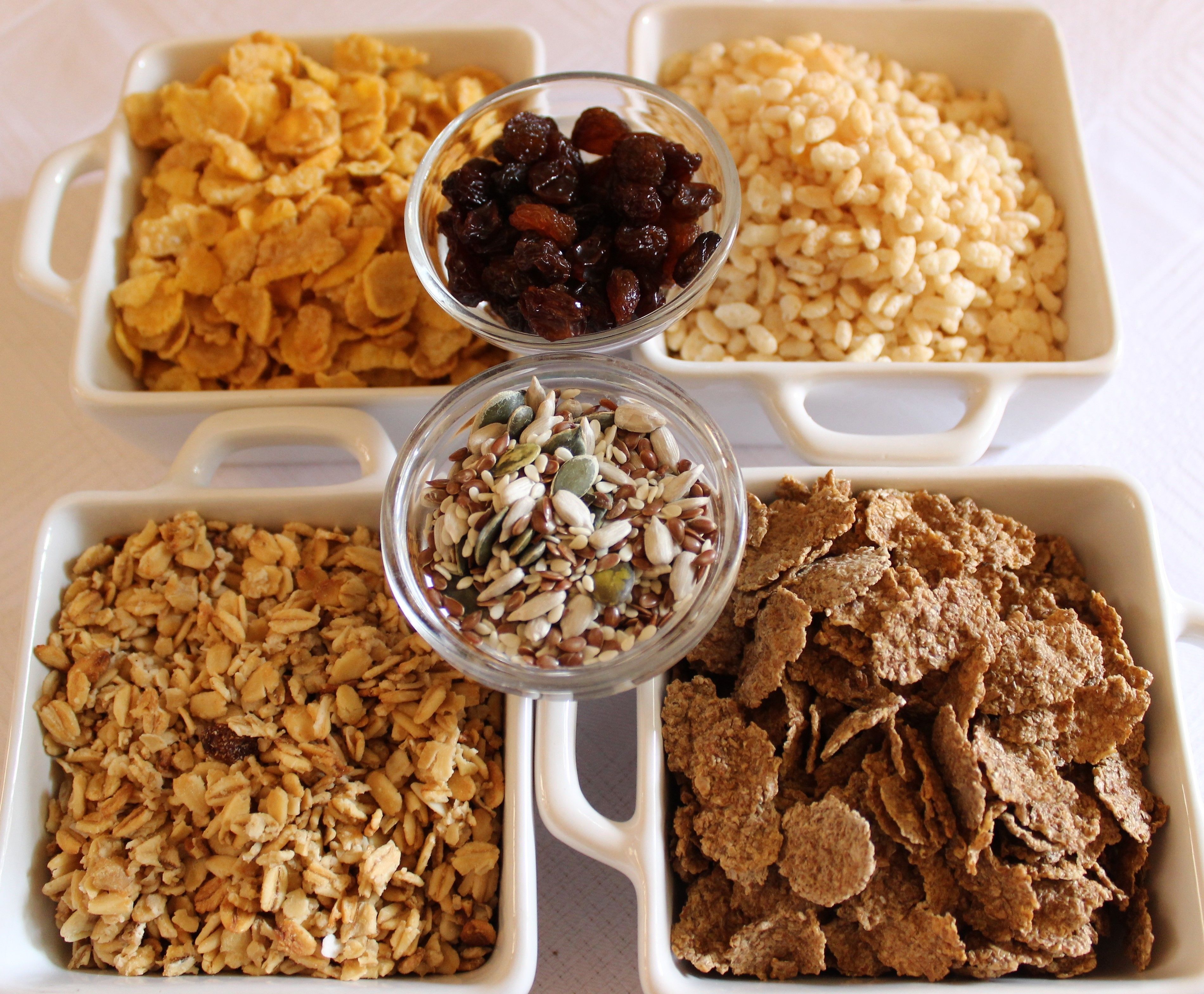 Four white ceramic dishes containing different types of cereal and nuts.