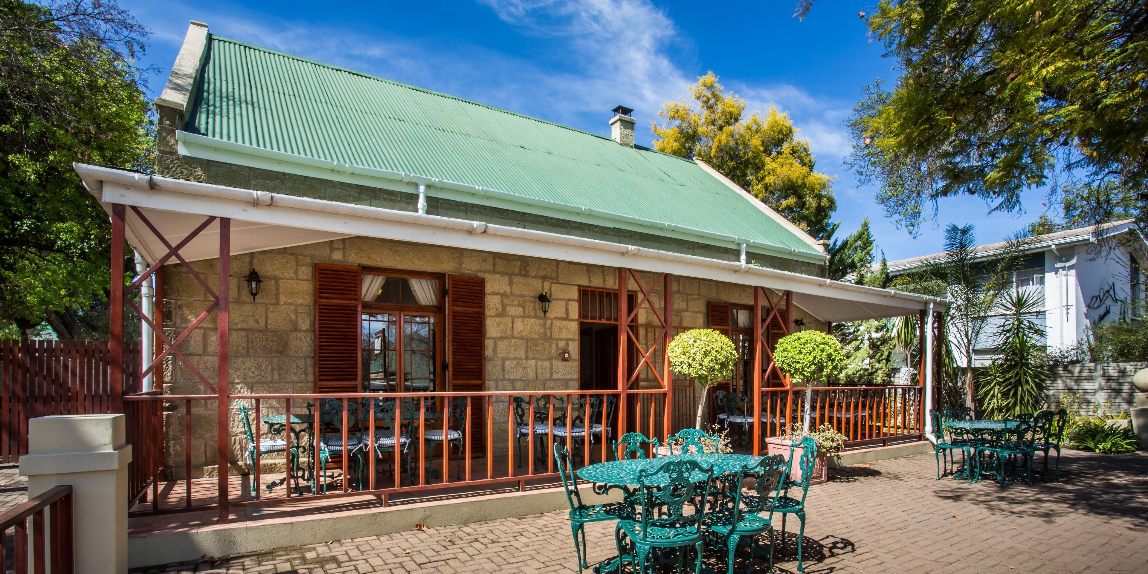 A building with a green roof, stone walls, and a covered patio area with tables and chairs.