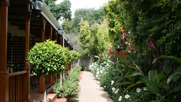 A brick pathway flanked by lush greenery and wooden structures.