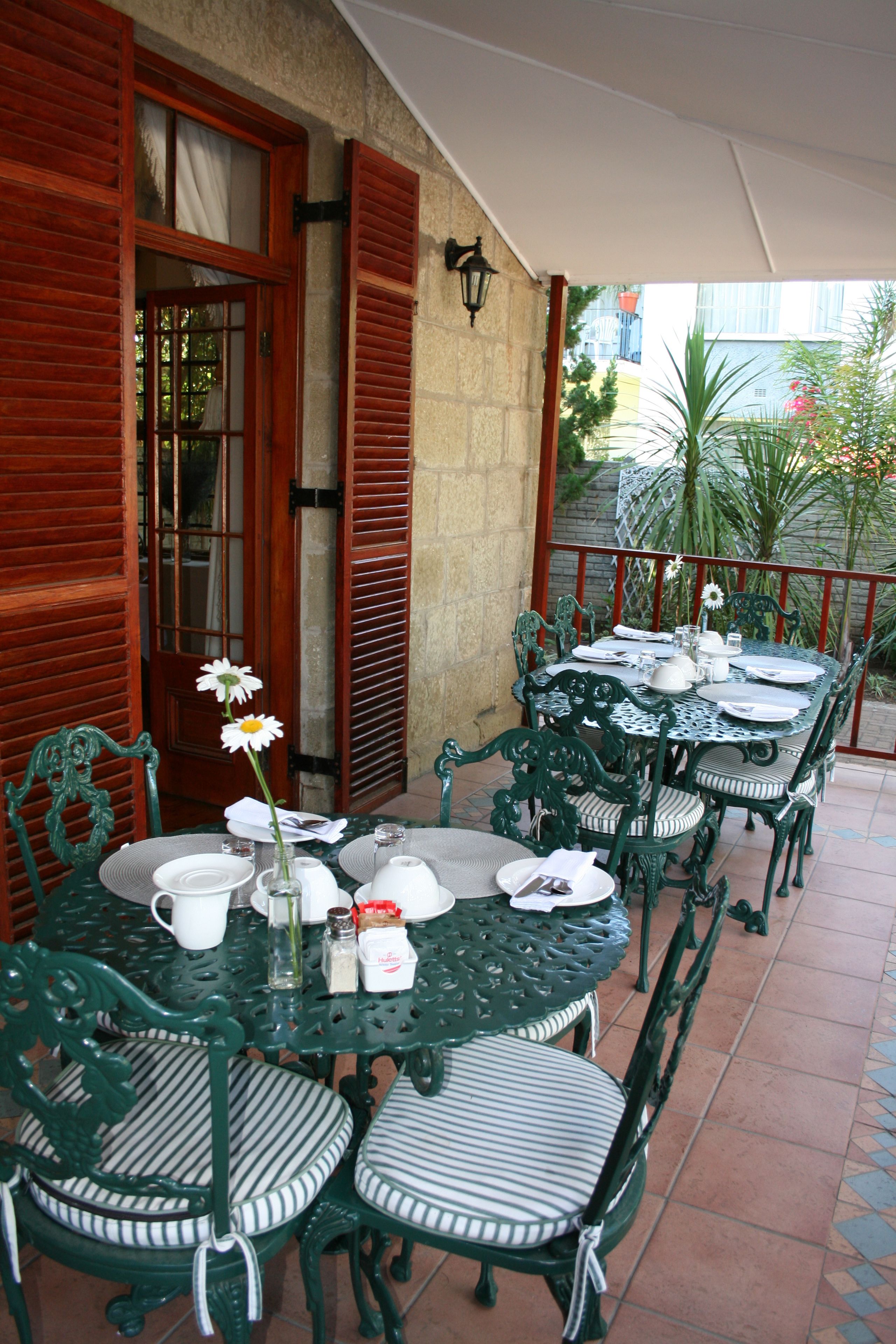 An outdoor dining area with a round table and chairs, a vase with a flower, and a view of the street and buildings in the background.