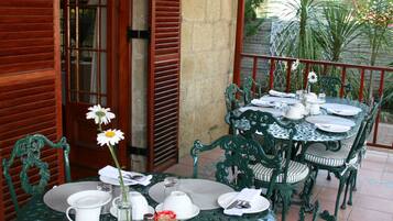 An outdoor dining area with a round table and chairs, a vase with a flower, and a view of the street and buildings in the background.