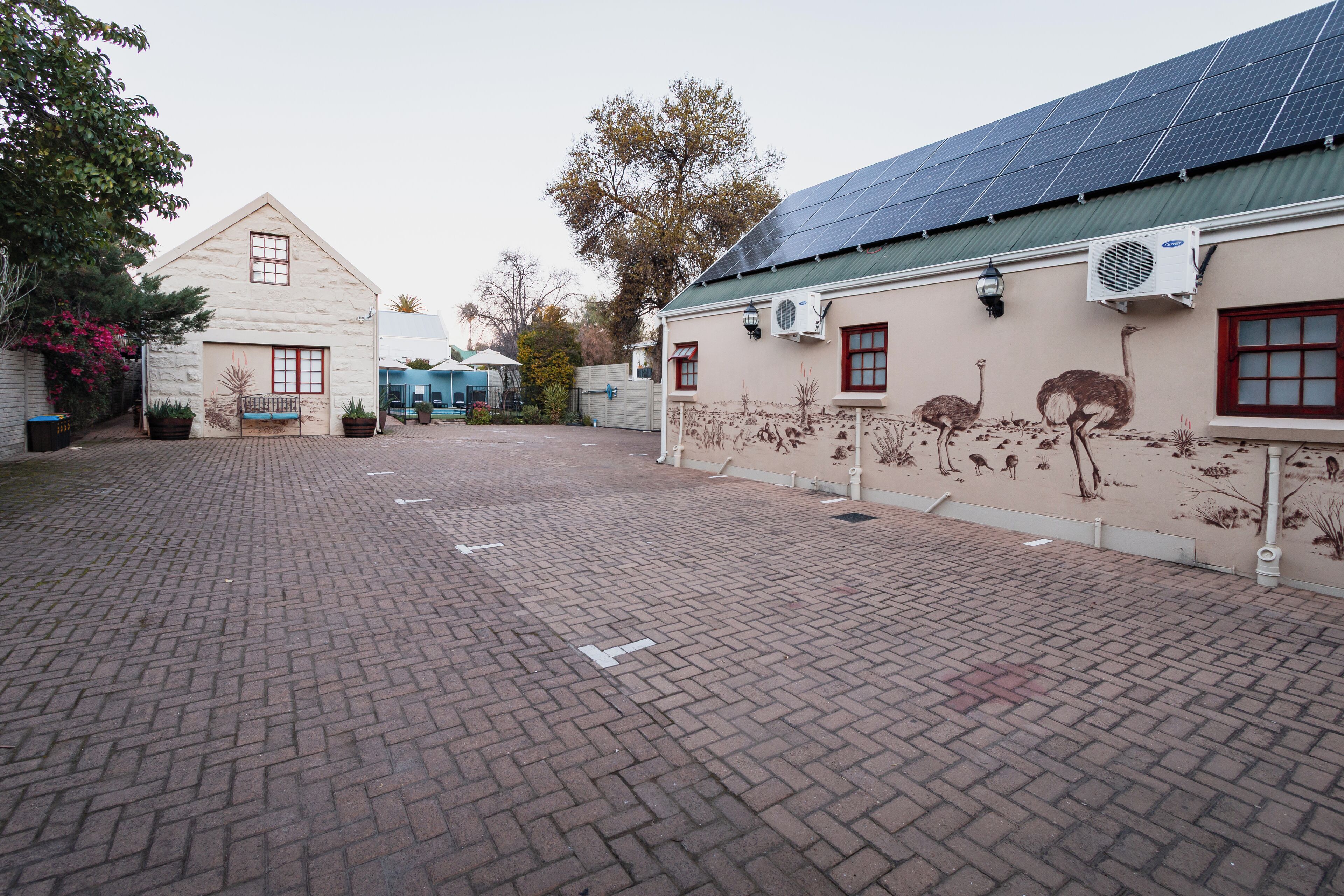 A courtyard with a brick floor, a building with a mural of ostriches, and solar panels on the roof.
