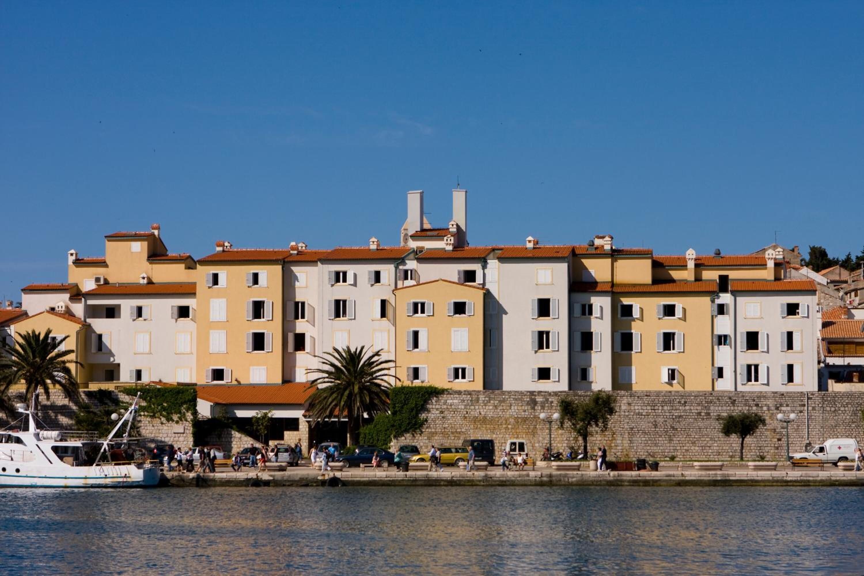 A waterfront building with multiple balconies, a stone wall, and a boat docked at the pier.