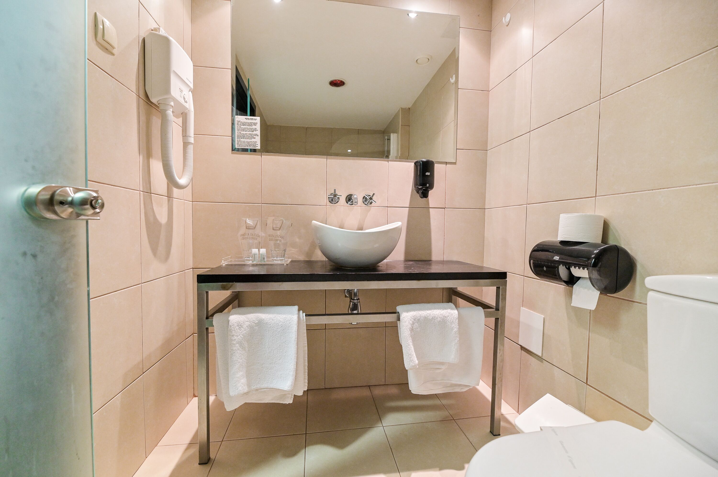 A modern bathroom with a large sink, a mirror, a toilet, and a towel rack.